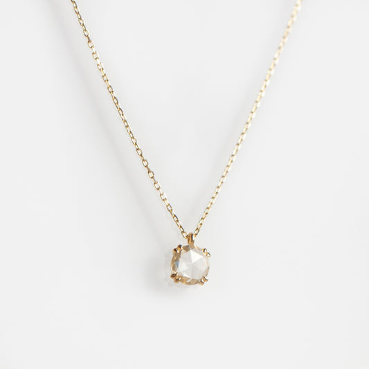 The Solid Gold Shimmering Gemstone Pendant Necklace Sample showcases a round, faceted white sapphire pendant on a delicate yellow gold chain, set against a plain white background.