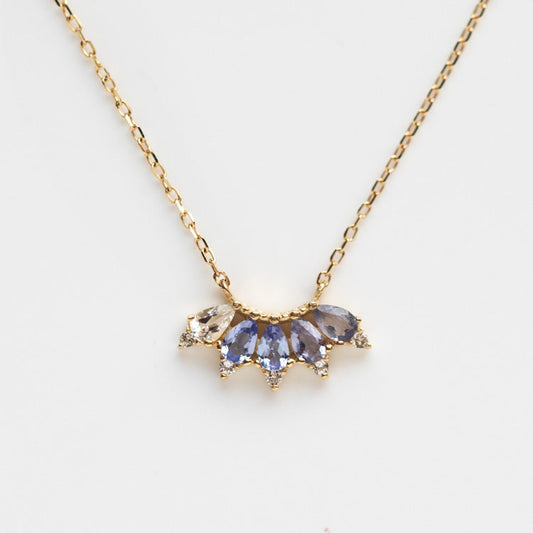 The Solid Gold Ombre Birthstone Necklace December Sample features a 9k yellow gold chain with a fan-shaped pendant adorned with five faceted blue and clear gemstones, accented by sparkling crystals. Photographed on a plain white background.