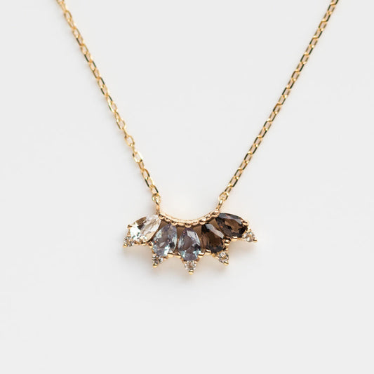 The Solid Gold Ombre Birthstone Necklace June Sample is a 9k yellow gold chain with a fan-shaped pendant, featuring five marquise-cut stones in clear, gray, and brown shades—ideal for those who love distinctive white topaz jewelry.