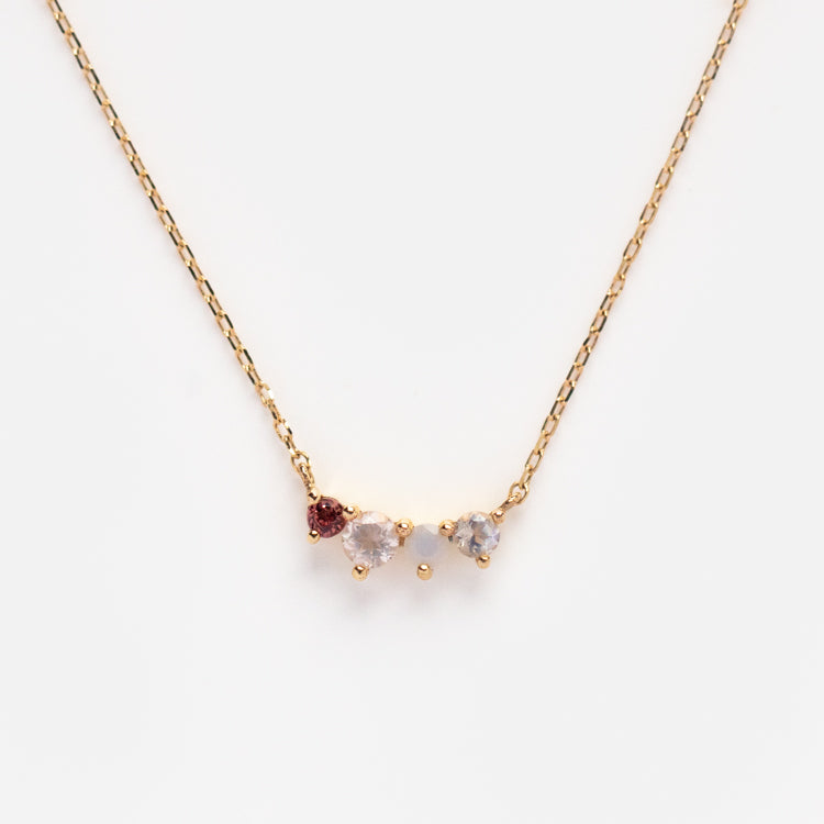 The Solid Gold Grow Acrostic Necklace Sample is a 9k yellow gold chain with a pendant of rose quartz, garnet, and a clear gemstone, shown against a plain white background.