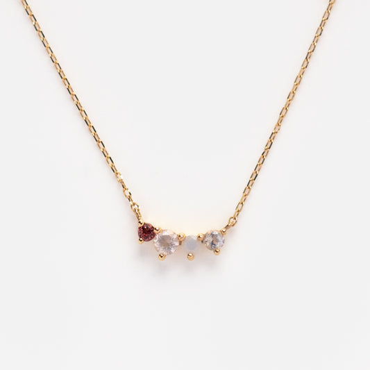 The Solid Gold Grow Acrostic Necklace Sample is a 9k yellow gold chain with a pendant of rose quartz, garnet, and a clear gemstone, shown against a plain white background.