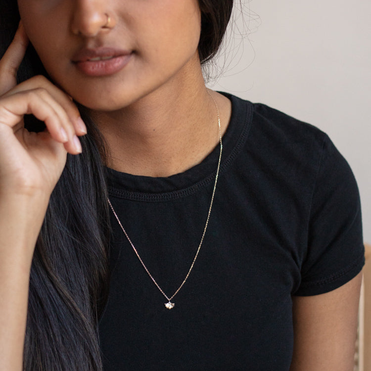 A woman wearing a black t-shirt rests her hand near her face, showcasing the Solid Gold Ginkgo Leaf Diamond Necklace. Only the lower half of her face and torso are visible.