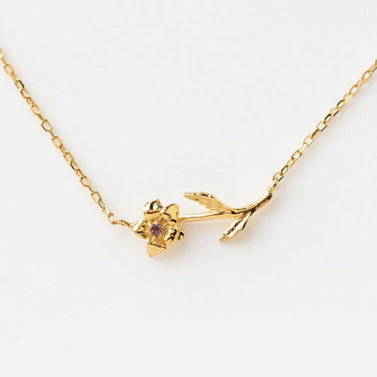 The Solid Gold Birth Flower Necklace February Sample features a 9k yellow gold flower pendant with a natural amethyst center and two leaf accents, beautifully displayed on a white background.