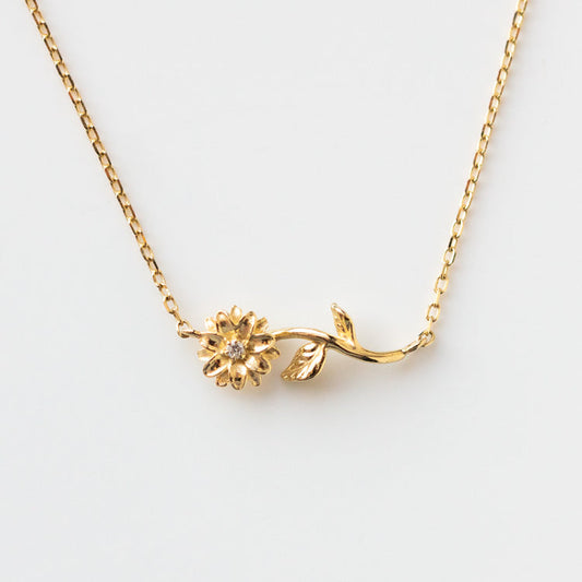The Solid Gold Birth Flower April Necklace Sample is a delicate 9k yellow gold pendant with a small flower and leaf on a curved stem, shown against a plain white background.