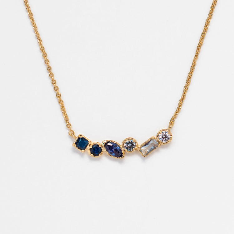 The Shades of You Ombre Birthstone Necklace features a delicate gold chain with five assorted blue, clear, and purple gemstones in various shapes set in gold bezels. A perfect personalized gift for any occasion.