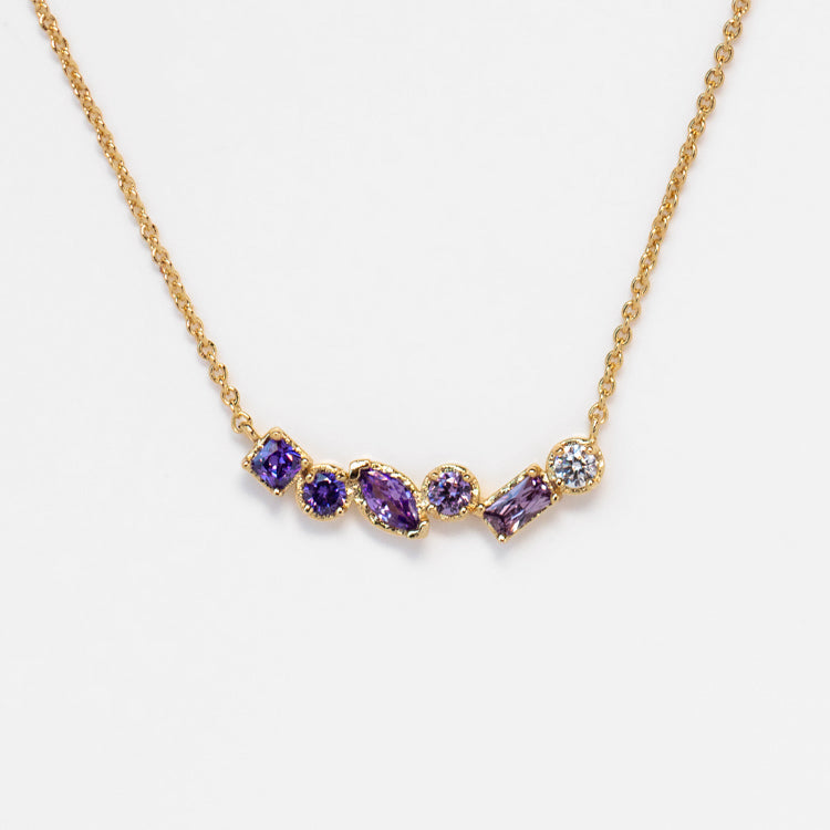 The Shades of You Ombre Birthstone Necklace features seven purple and clear gemstones of assorted shapes and sizes, set in a row on an elegant gold pendant.
