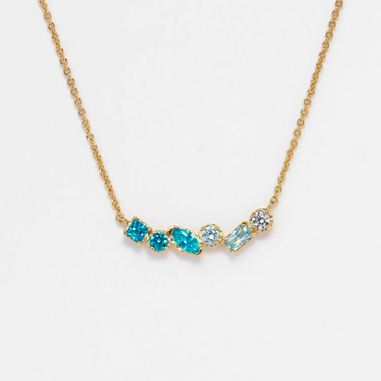 The Shades of You Ombre Birthstone Necklace showcases five ombre blue gemstones—oval, round, and rectangular—set in gold and arranged in a row, creating a stunning effect against a white background.
