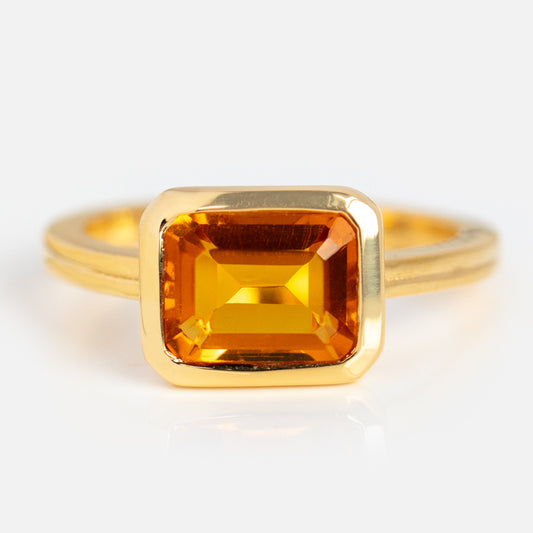 Exclusive to Local Eclectic, the East West Bold Bezel Set Ring features a gold-plated setting with a rectangular emerald-cut yellow-orange gemstone, beautifully displayed on a plain white background.