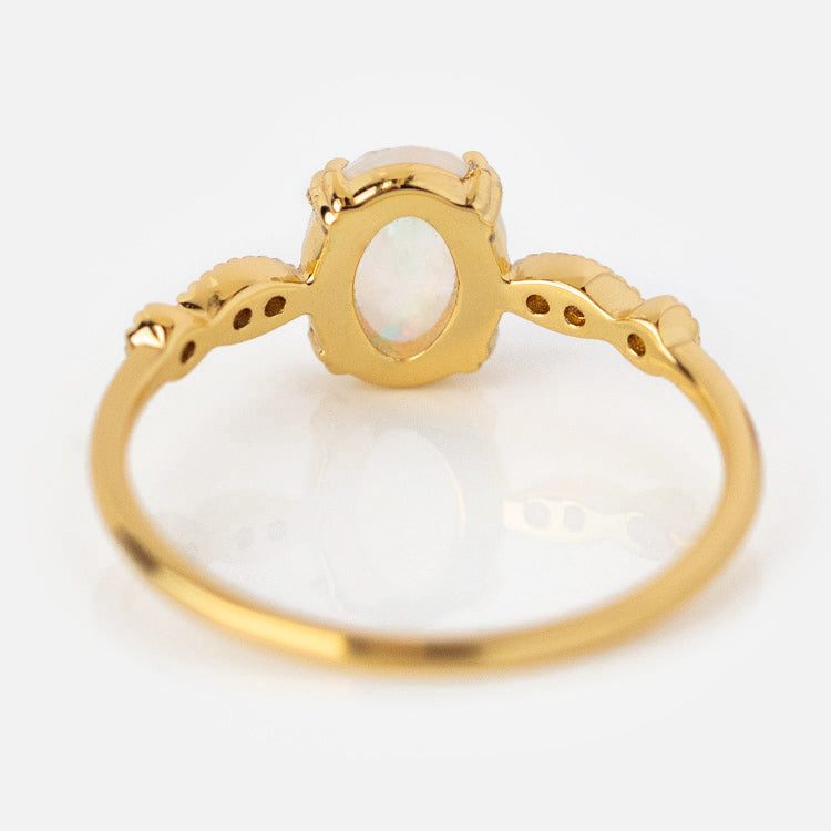 The Opal Fire Ring features a thin, ornate gold band with an oval simulated opal gemstone at its center—a stunning statement piece for any occasion.