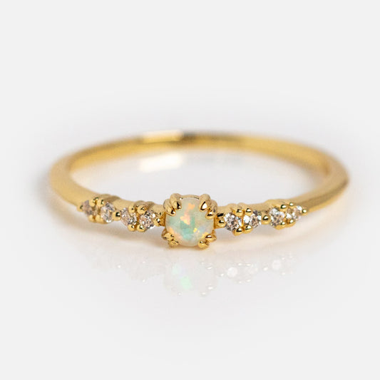 The Opal Sparkle Ring showcases an oval simulated opal centerpiece accented by sparkling cubic zirconia stones on each side, set against a plain white background.