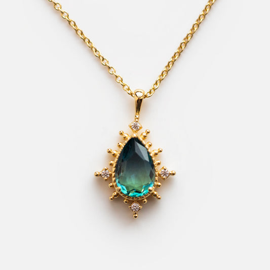 The Nightfall Tourmaline Pendant Necklace showcases a teardrop blue-green gemstone, small round white stones, and 14k gold vermeil accents on a white background.