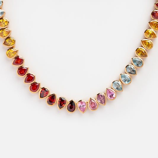 The Bold Bezel Set Tennis Necklace Multi Sample is a 14k yellow gold plated piece featuring pear-shaped cubic zirconia in red, yellow, blue, and pink, arranged symmetrically for a vibrant look.