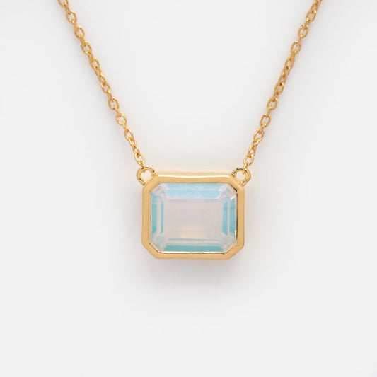 The Around the Sun Birthstone Necklace October Sample showcases a rectangular, faceted colored glass gem set in a yellow gold plated pendant on a gold chain, displayed against a white background.
