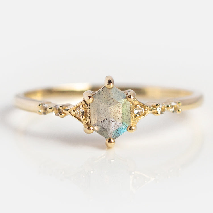 The Solid Gold Mystic Labradorite Hexagon Ring for Protection features a 9k yellow gold band with a central iridescent labradorite hexagon and small round accent stones, shown on a clean white background.