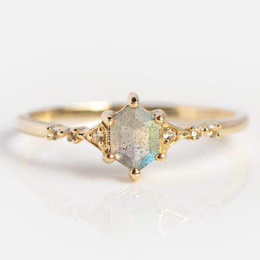 The Solid Gold Mystic Labradorite Hexagon Ring for Protection features a 9k yellow gold band with a central iridescent labradorite hexagon and small round accent stones, shown on a clean white background.