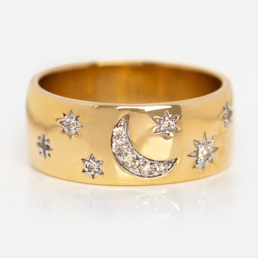 The Solid Gold Diamond Night Sky Cigar Band, exclusive to Local Eclectic, is a wide gold ring featuring a crescent moon and sparkling diamond stars on a plain background.