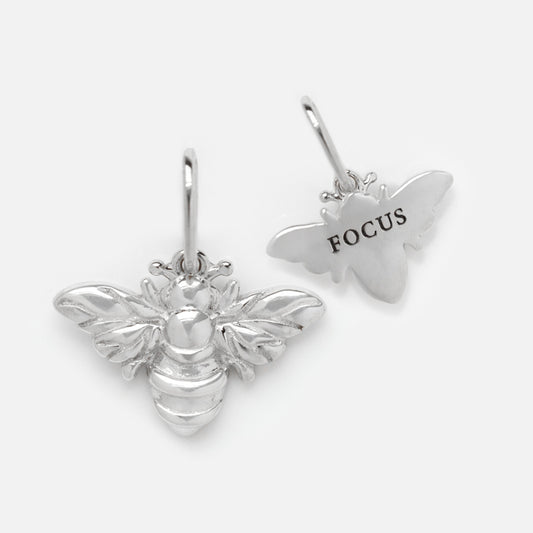 Two silver bee-shaped charms—one shows the front, the other has FOCUS engraved on the back. Each has a loop for attaching to jewelry. These are perfect Solid Gold Nature Charms in White Gold for any nature-inspired accessory.