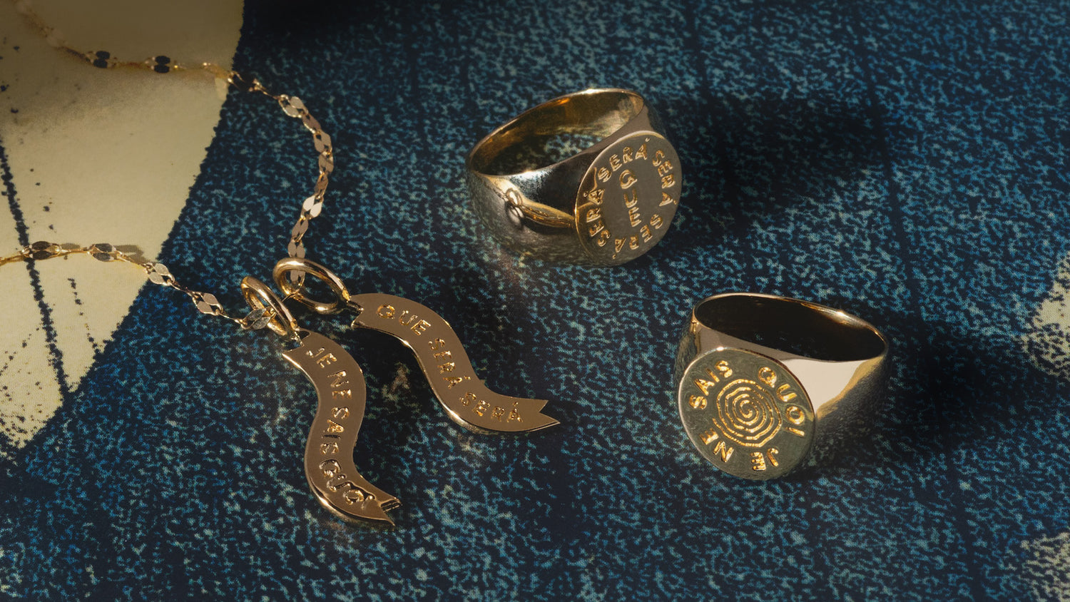 Gold jewelry including a necklace and two rings on a textured blue surface