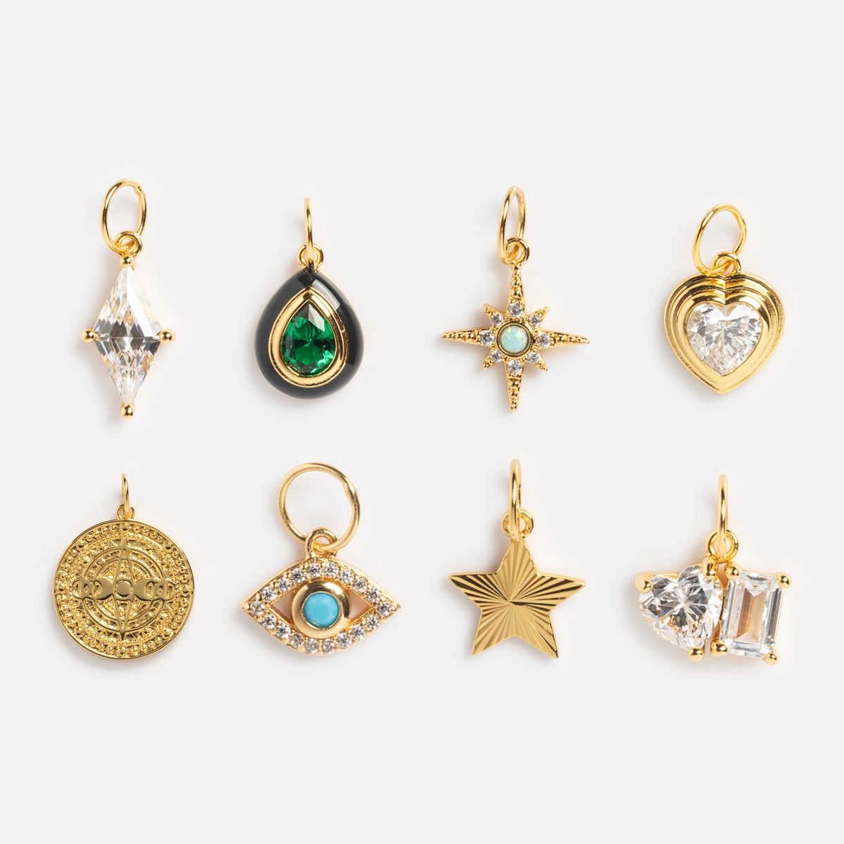 Eight yellow gold plated charms from Charms by Jurate JLA, featuring a simulated diamond, teardrop, starburst, heart, round coin, eye, star, and a cluster of two clear gemstones arranged in two rows on a white background.