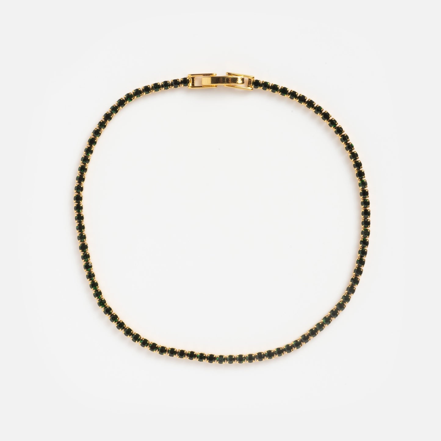 The Emerald CZ Tennis Bracelet Sample features a delicate gold chain with small green emerald cubic zirconia stones set evenly along its length, displayed in a circular shape on a white background.
