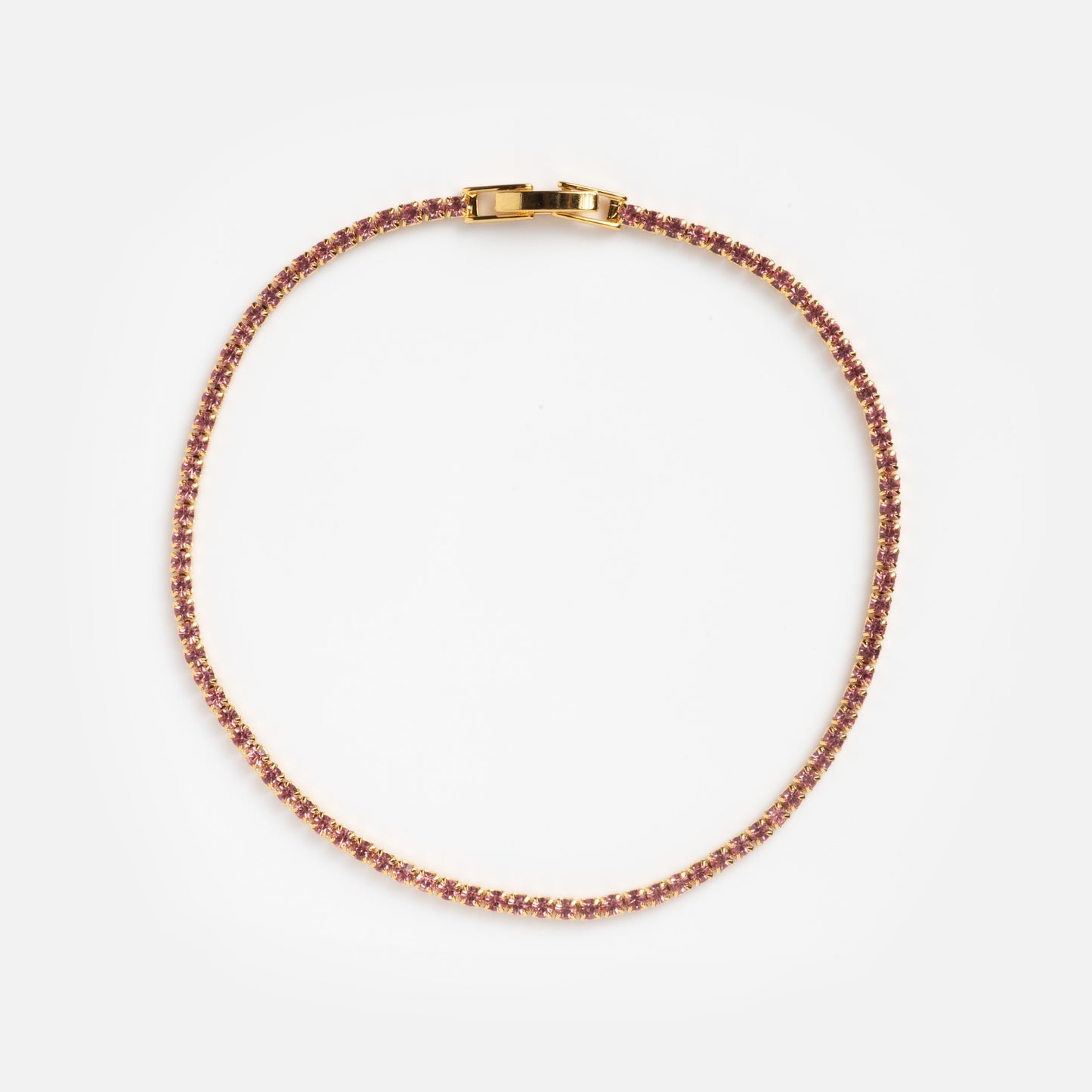 The Pink CZ Tennis Bracelet Sample features a delicate gold chain with small pink gemstones and a rectangular clasp, displayed in a circular shape on a plain white background.