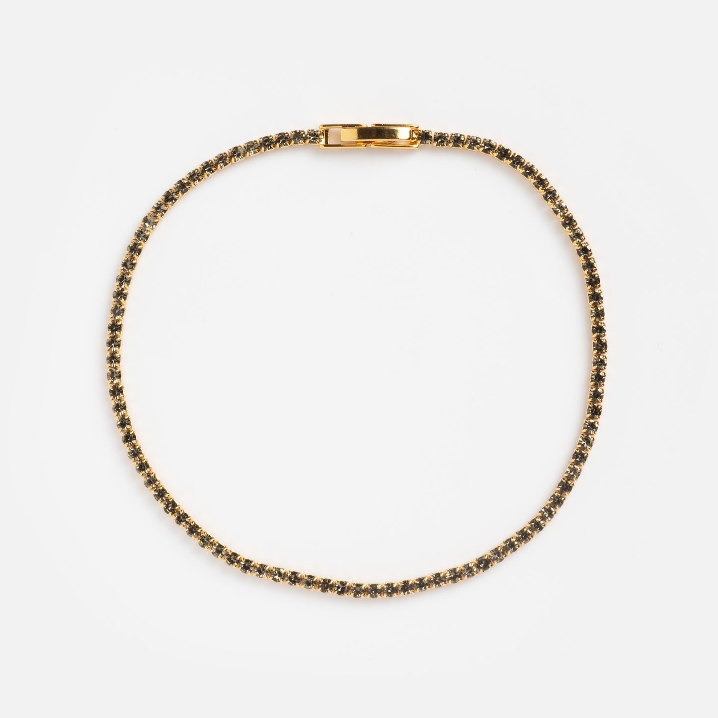 The Black CZ Tennis Bracelet Sample features small, evenly spaced dark gemstones set in gold, arranged in a circle on a plain white background with the clasp visible at the top.
