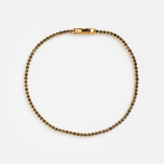 The Black CZ Tennis Bracelet Sample features small, evenly spaced dark gemstones set in gold, arranged in a circle on a plain white background with the clasp visible at the top.