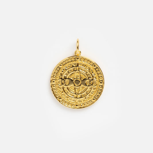 The Charms by Jurate JLA is a round yellow gold plated pendant with raised geometric and circular patterns, a small top loop for attaching to a chain, and is ideal for layering with other charms.