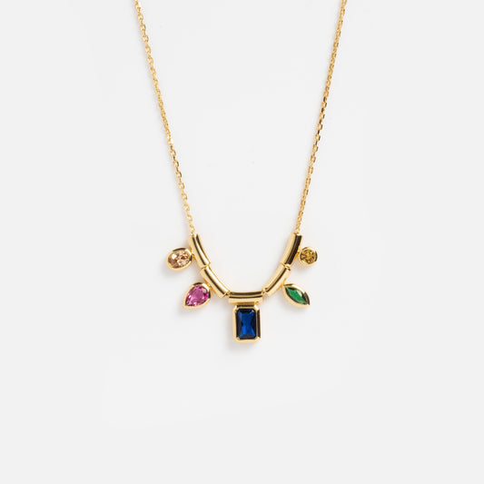 The Technicolor Gem Drop Necklace features a fine gold chain with a central rectangular blue gemstone pendant and four dangling charms in pink, green, and yellow gemstones.