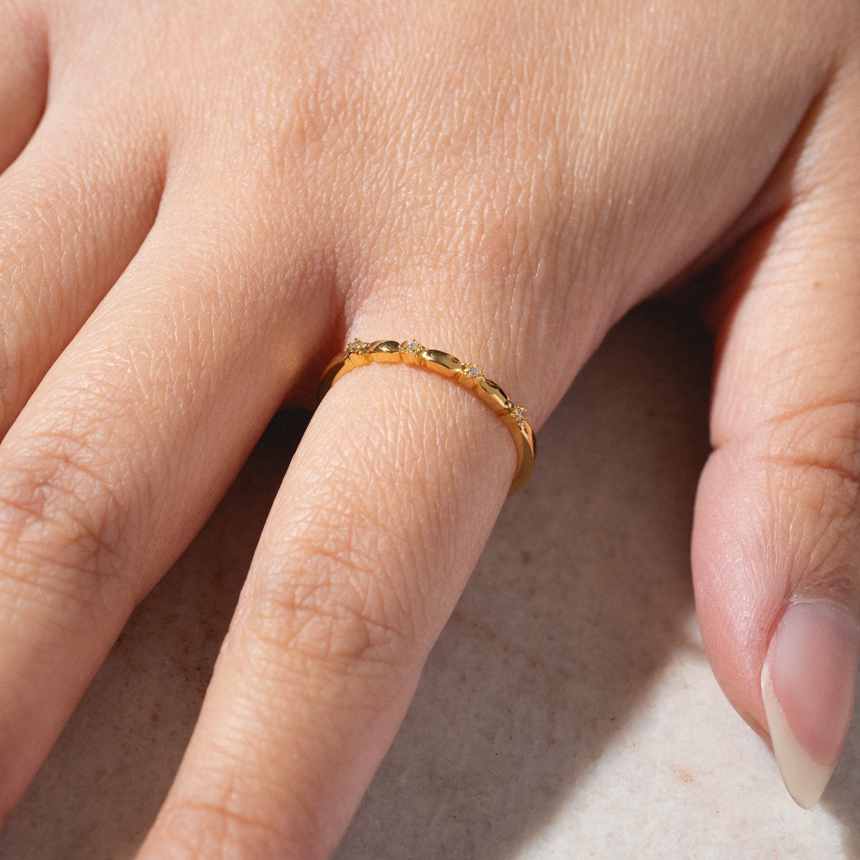 A hand wearing the Starry Stacking Band—a gold, textured ring—on the ring finger rests on a light surface. The nails are natural and neatly manicured.