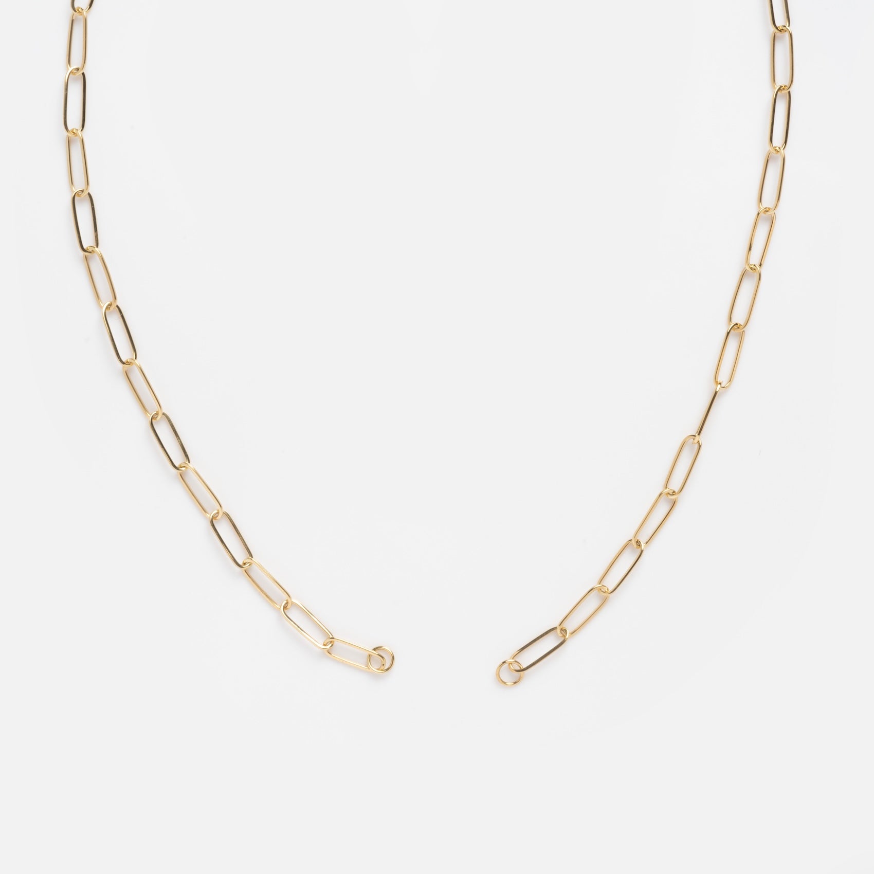 The Solid Gold Perfect Start Charm Holder Necklace features delicate 9k gold elongated oval links in a gentle curve, displayed on a white background with open ends revealing the clasp—ideal for showcasing your favorite charms.