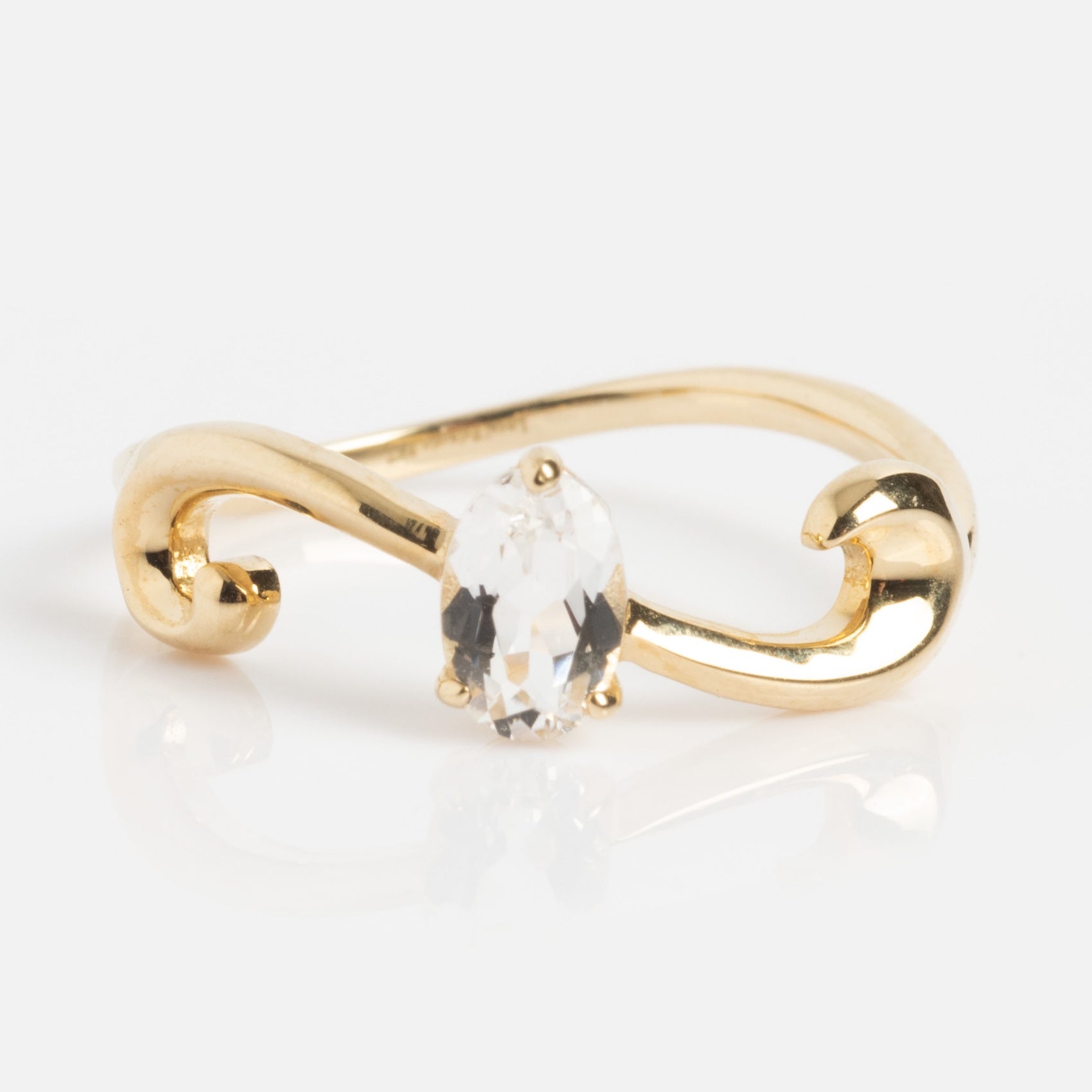 The Solid Gold White Topaz Ring Sample Size 7 features a 9k yellow gold swirling band and a clear, 4x6mm oval-cut white topaz centerpiece, shown on a white background.