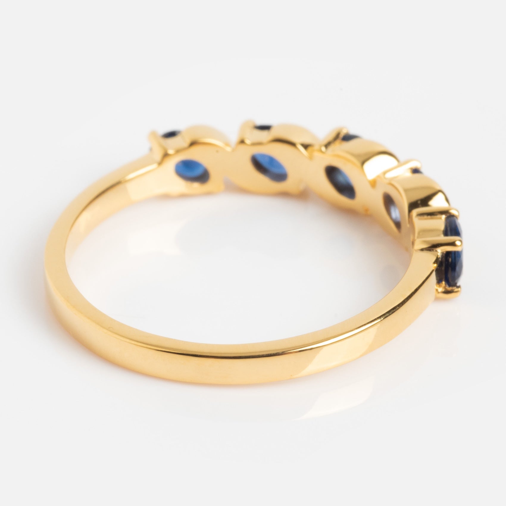The Blue Twist Vintage Inspired Ring features a row of oval blue gemstones set in prongs along a gold band, displayed from an angled side view on a plain white background.