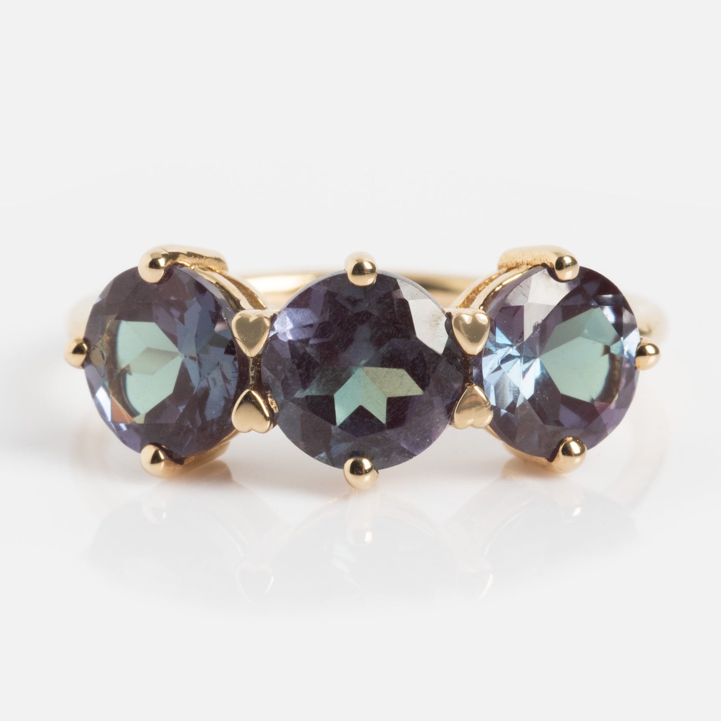 A One of a Kind 14k Heart Prong Lab Alexandrite Trio Ring with three round purple-blue lab alexandrites set in heart-shaped prongs on a plain gold band, shown against a white background.