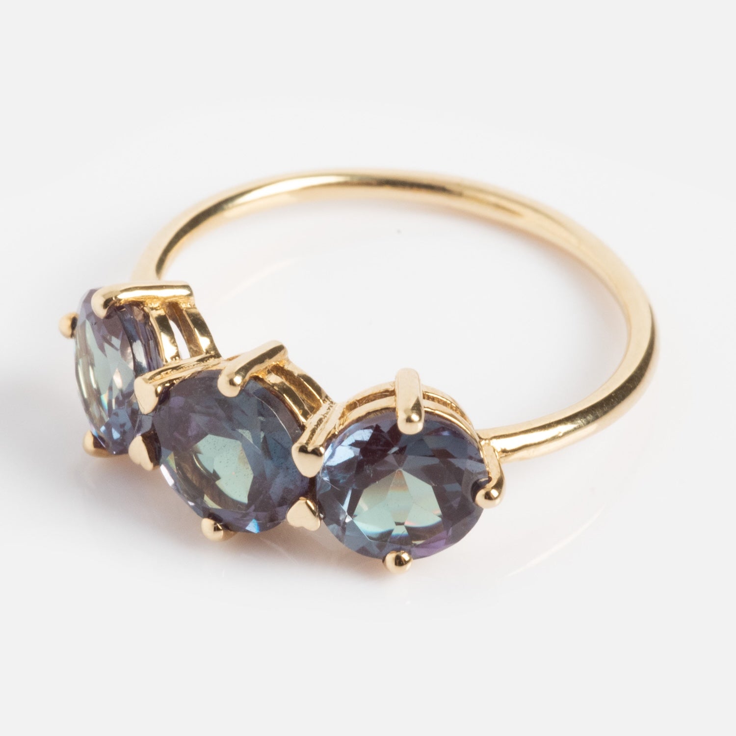 The One of a Kind 14k Heart Prong Lab Alexandrite Trio Ring features three round blue-purple lab alexandrites in heart prongs on a simple gold band, shown on a white background.