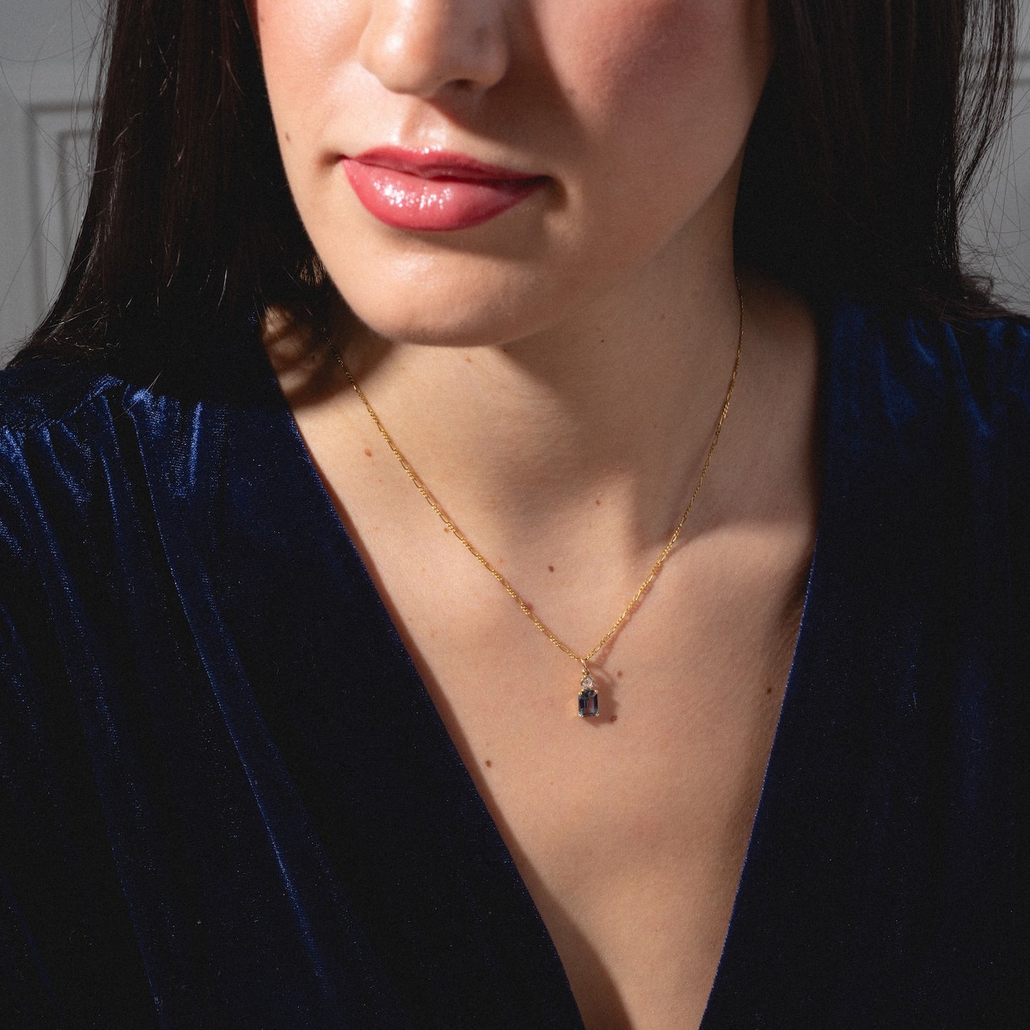 A woman wears a dark blue velvet top and the One of a Kind 14k Lab Alexandrite and Diamond Charm necklace. Her head is slightly turned, lips glossy pink, with a softly lit, blurred background.