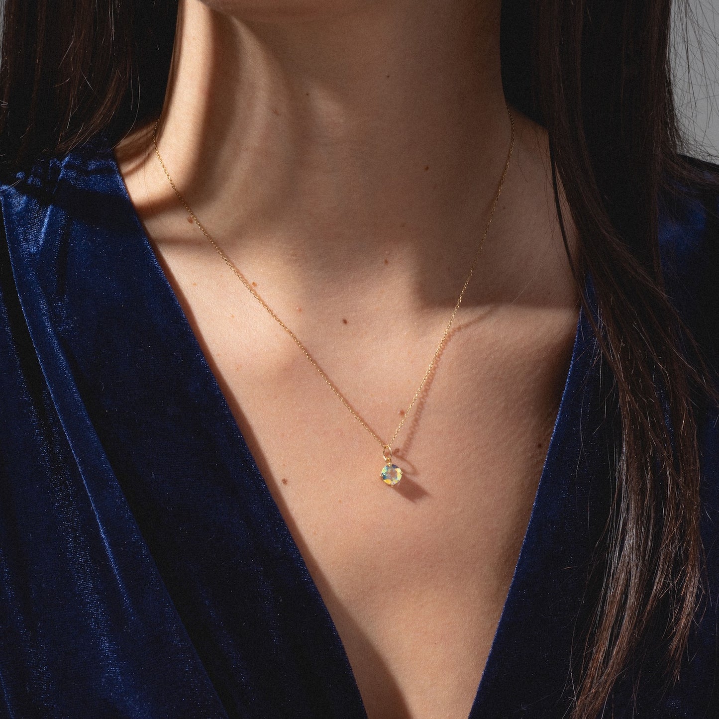 A woman wears a deep blue velvet top and the One of a Kind 14k Round Angel Aura Charm necklace. The image is cropped to highlight her neck, collarbone, and upper chest.