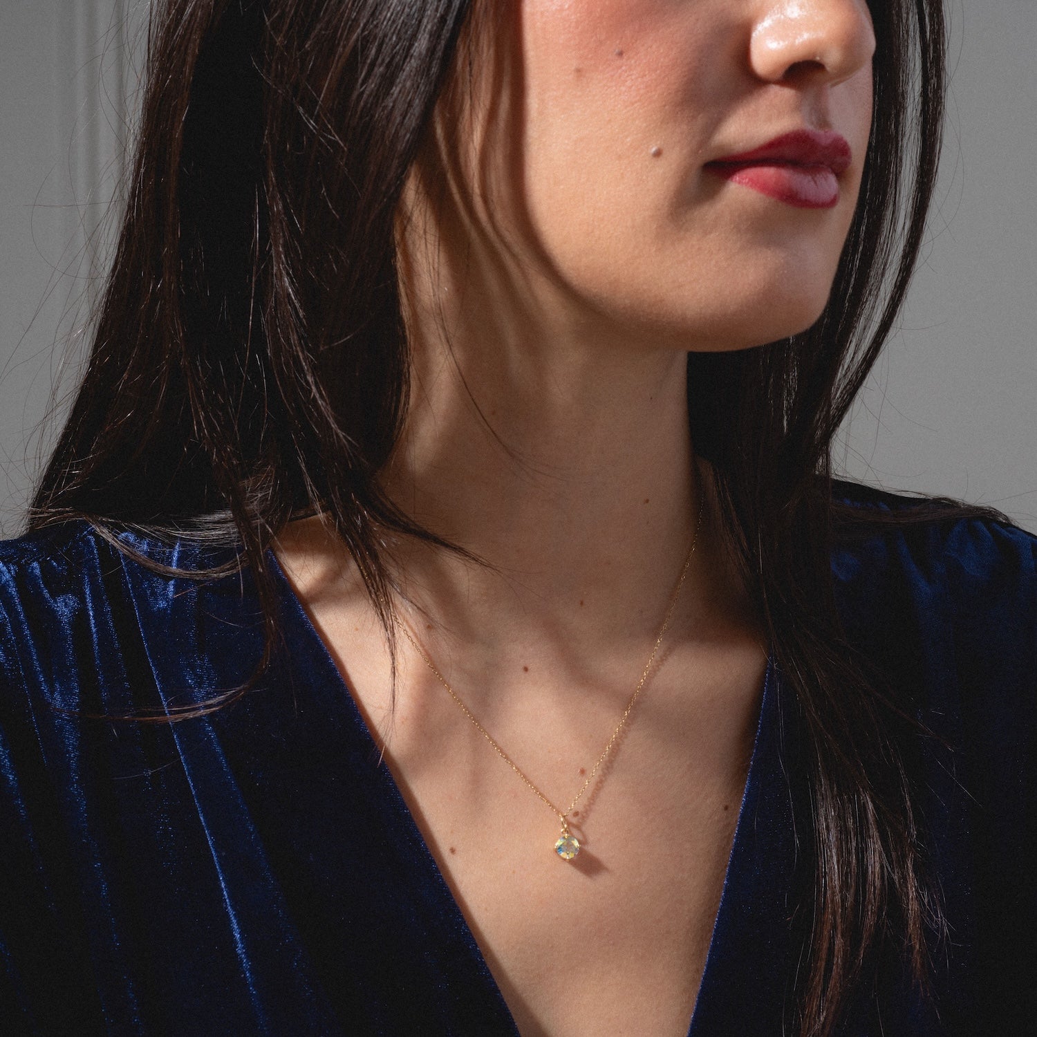 A woman with long dark hair wears a dark blue velvet top and the One of a Kind 14k Round Angel Aura Charm necklace. Only her lower face and upper chest are visible.