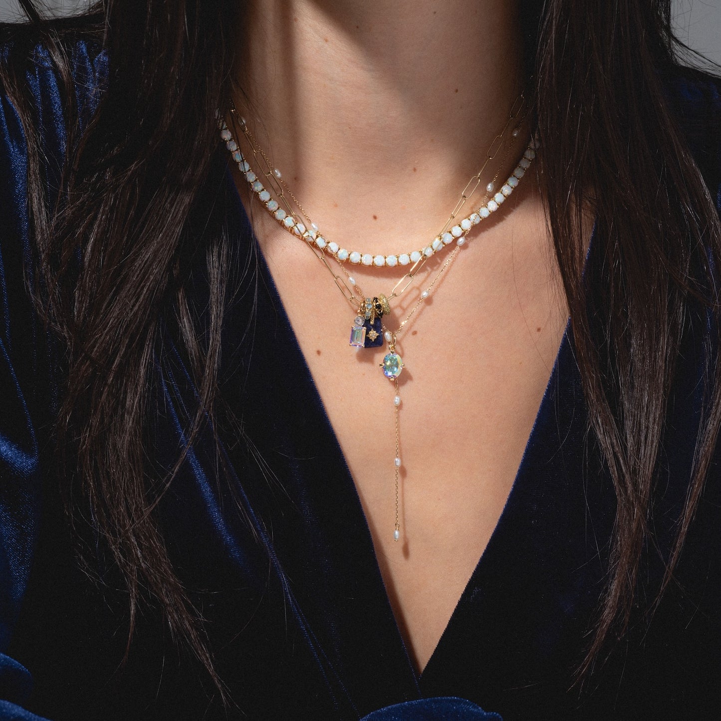 A woman wears a deep blue velvet top and layered gold necklaces, including the Solid Gold Pearl Lariat Necklace with star, crystal, and freshwater pearl accents, set against a neutral background.