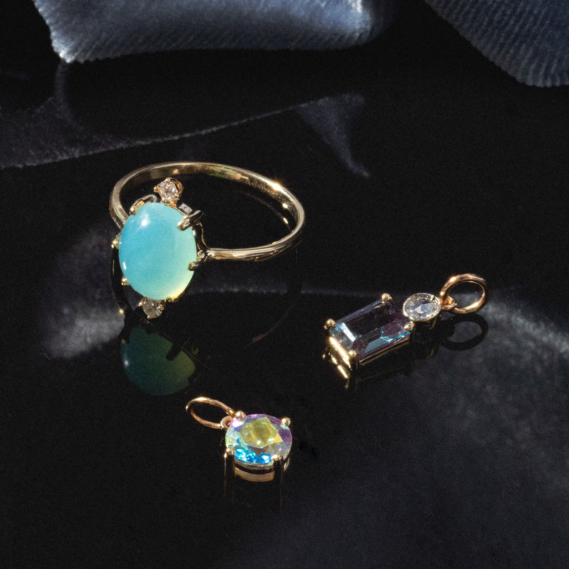 The One of a Kind 14k Peruvian Opal and Diamond Ring, featuring a large oval pale blue gemstone and sparkling diamonds, rests on a glossy black surface with soft blue fabric in the background.
