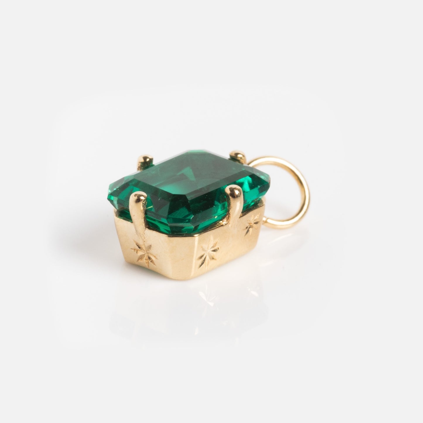 The One of a Kind 14k Lab Emerald Charm features hand-engraved details and an emerald-cut green gemstone, showcased against a plain white background.
