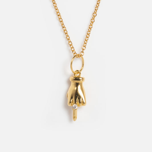 The Kiss Off Necklace features a 14k gold plated hand pendant pointing downward with an index finger tipped with a clear gemstone and finished in polished gold, displayed against a plain white background.