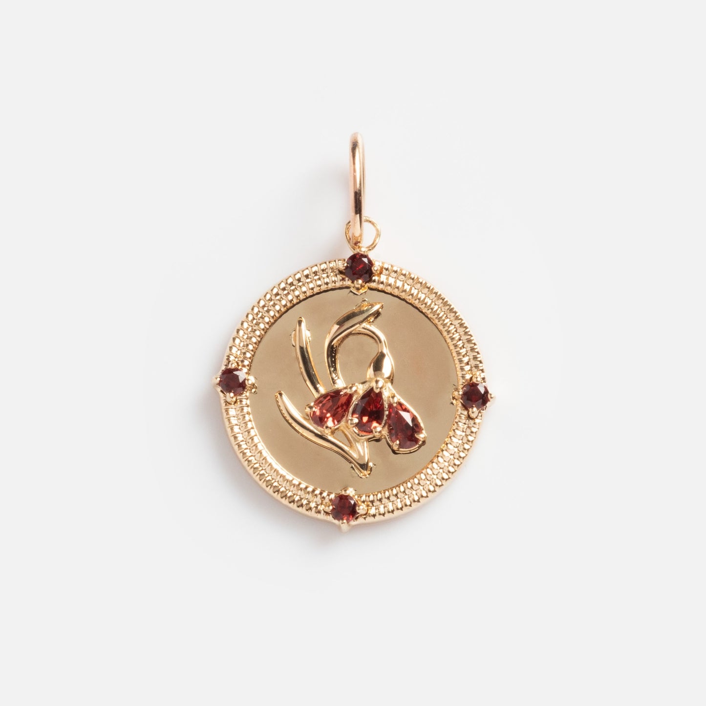 The Solid Gold 2026 January Capsule Vintage Inspired Garnet Coin Charm features a raised flower design with four garnet stones around the textured edge and a top loop for attaching to a necklace or bracelet, shown against a white background.
