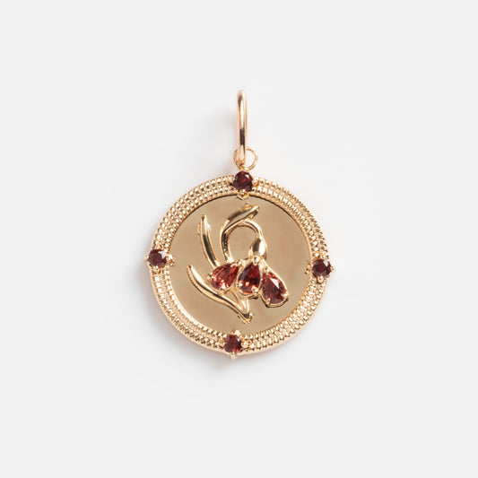 The Solid Gold 2026 January Capsule Vintage Inspired Garnet Coin Charm features a raised flower design with four garnet stones around the textured edge and a top loop for attaching to a necklace or bracelet, shown against a white background.