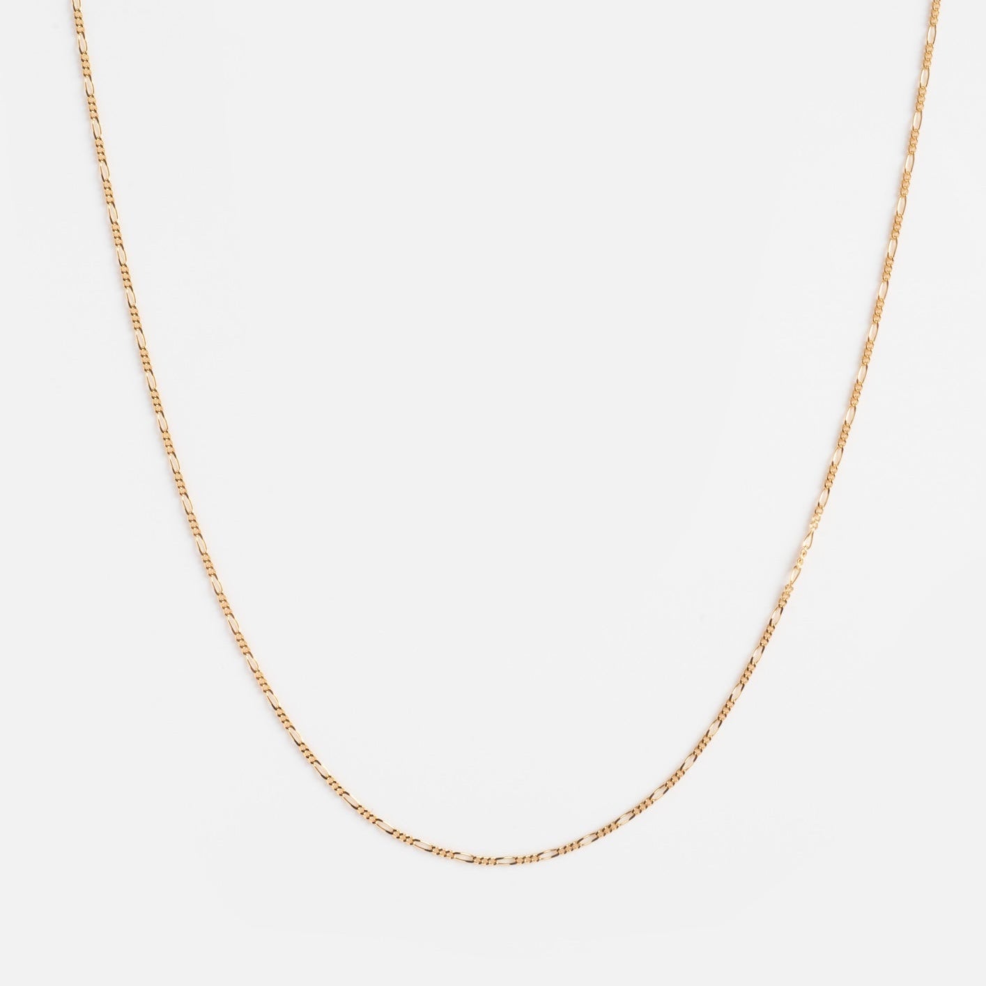 The Solid Gold Figaro Chain is a delicate, thin 9k yellow gold necklace with a subtle shine and simple design, shown on a plain white background. Perfect for layering in your favorite necklace stack.