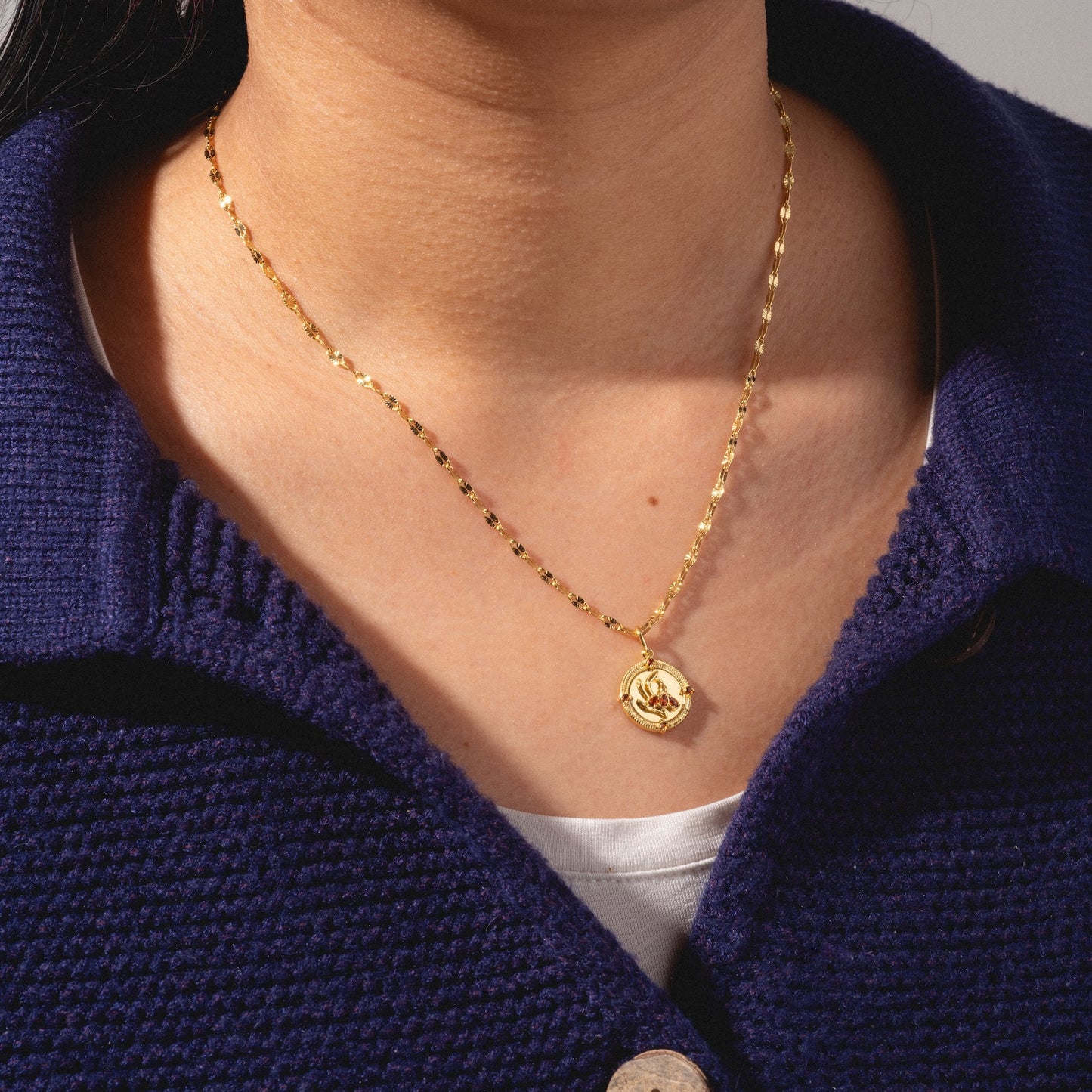 A close-up of a person wearing the 2026 January Capsule Vintage Inspired Garnet Coin Charm necklace, paired with a navy textured jacket and white shirt—a Local Eclectic exclusive.