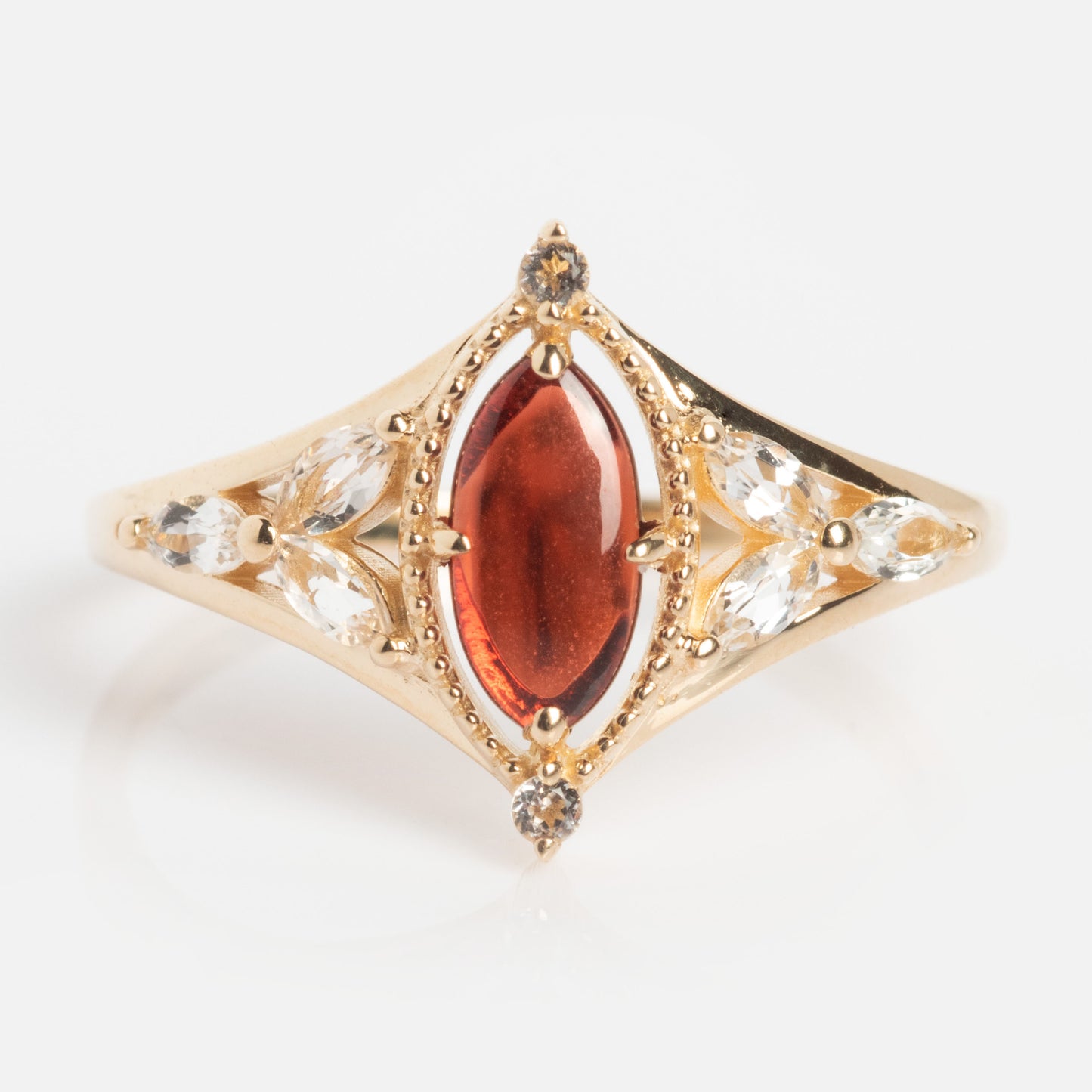 The Solid Gold 2026 January Capsule Art Deco Garnet Ring features a marquise-cut red garnet center, six smaller clear marquise stones, and decorative gold beading on each side, all set against a white background.