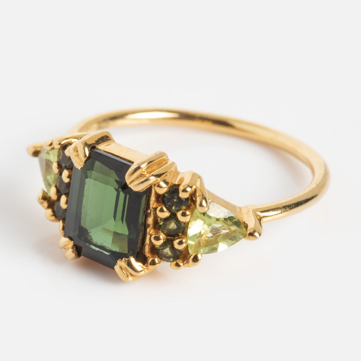 The Green with Envy Topaz and Peridot Regal Ring is a 14k gold vermeil ring showcasing a large, square-cut green topaz flanked by two triangular peridots on each side, set against a plain white background.