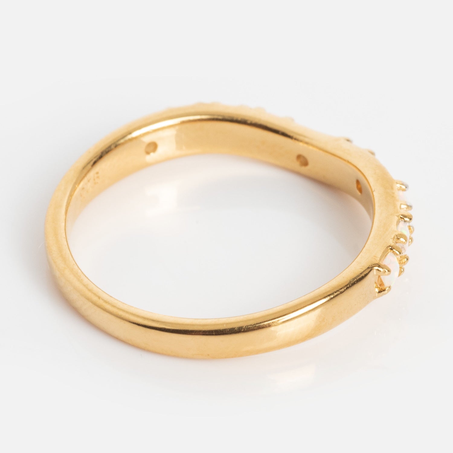 An Opal Stacking Wave Ring is photographed on a plain white background, viewed from the side to display its smooth gold band and small prongs on one side designed for setting stones.
