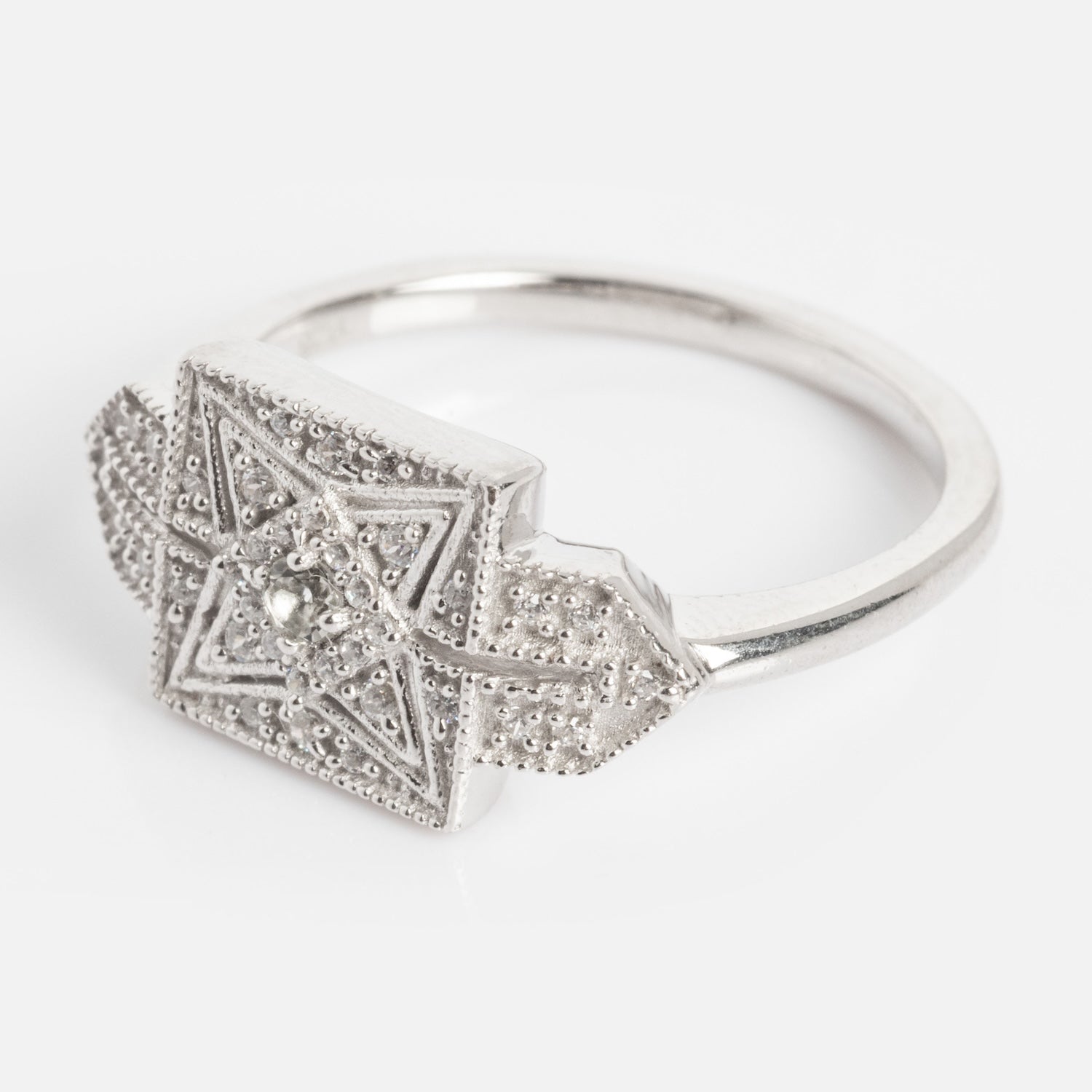 The Art Deco Inspired Statement Ring is a silver ring with a square top, featuring an intricate geometric star pattern and small raised dots, shown on a plain white background.
